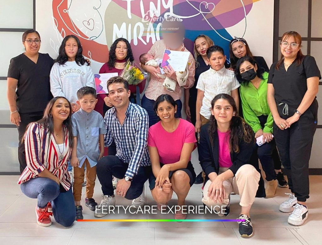 Grupo de personas, incluidos niños, reunidos frente al mural de FertyCare, representando la experiencia de subrogación y apoyo familiar.