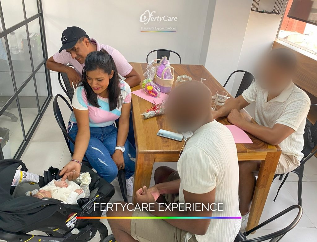 Familia conversando alrededor de una mesa mientras cuidan a un bebé en su portabebé, en las oficinas de FertyCare, representando la experiencia de subrogación.