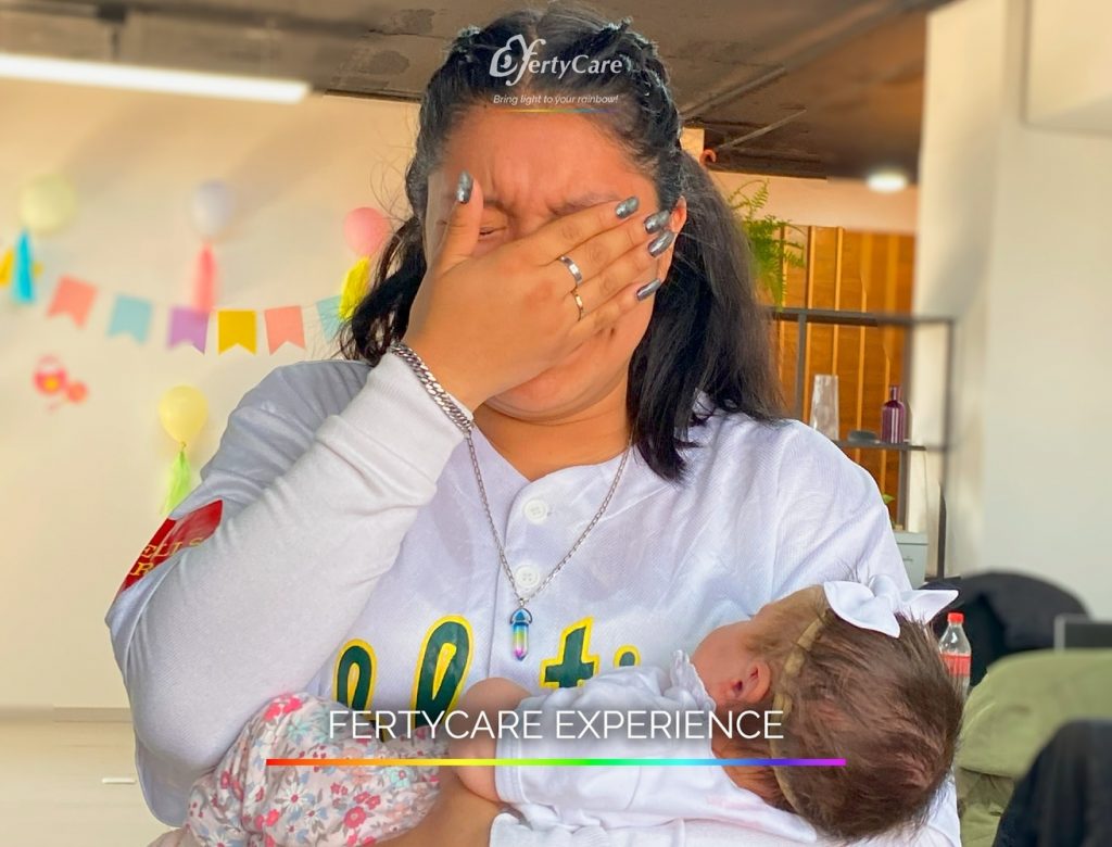 Mujer llorando de emoción mientras sostiene a su bebé con un lazo blanco, representando la experiencia de subrogación en FertyCare.